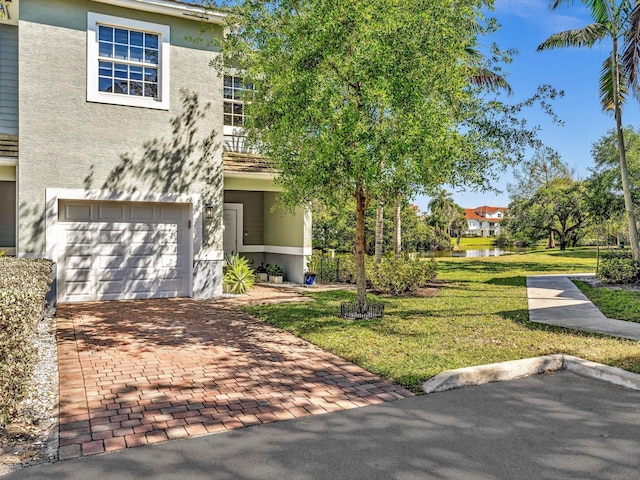 view of front of property featuring stucco siding, decorative driveway, a garage, and a front lawn