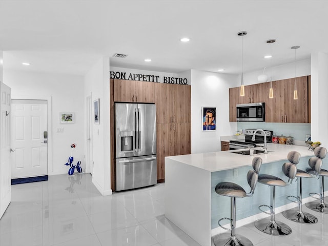 kitchen with a peninsula, a kitchen breakfast bar, brown cabinets, and appliances with stainless steel finishes