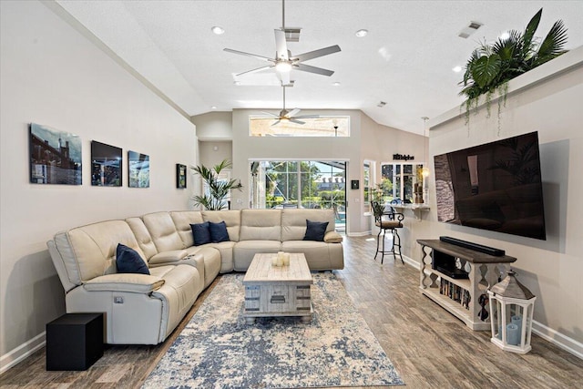 living area with baseboards, wood finished floors, visible vents, and high vaulted ceiling