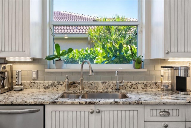 kitchen featuring stainless steel dishwasher, plenty of natural light, white cabinetry, and a sink