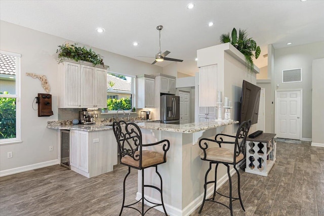 kitchen with visible vents, stainless steel fridge with ice dispenser, light stone counters, a kitchen breakfast bar, and a peninsula