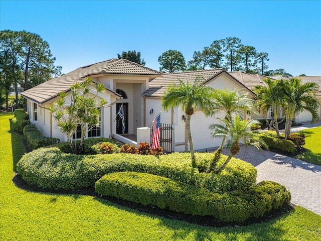 view of front facade with stucco siding, a front lawn, a tile roof, decorative driveway, and a garage