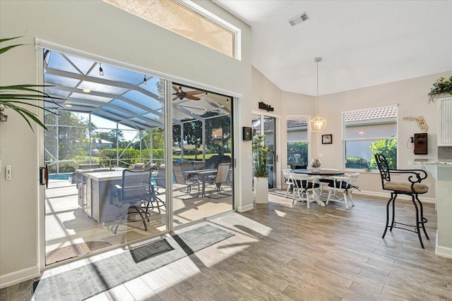 interior space with light wood finished floors, visible vents, baseboards, a sunroom, and high vaulted ceiling