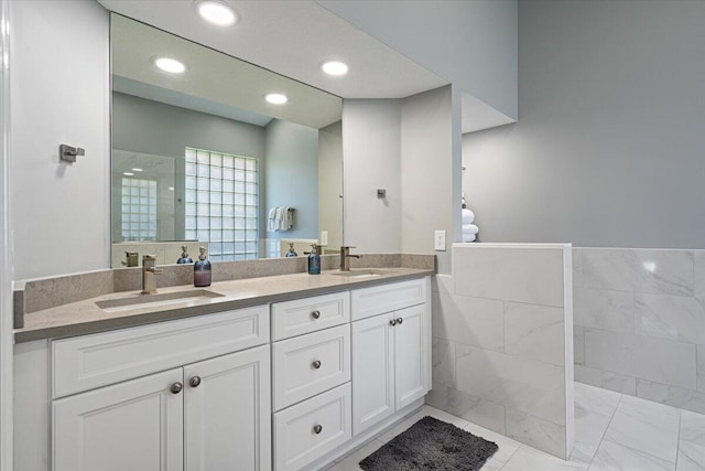 full bath with double vanity, recessed lighting, tile walls, and a sink