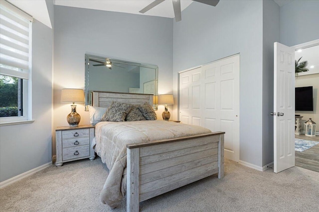 bedroom with light carpet, a ceiling fan, a closet, a high ceiling, and baseboards