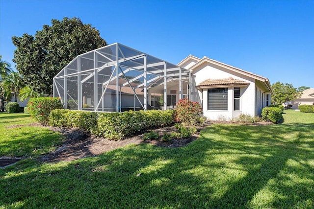 rear view of property featuring glass enclosure, a tile roof, a yard, and stucco siding