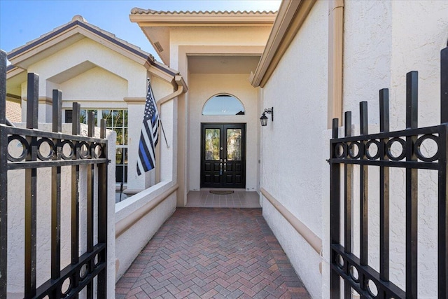 doorway to property featuring stucco siding, french doors, and fence