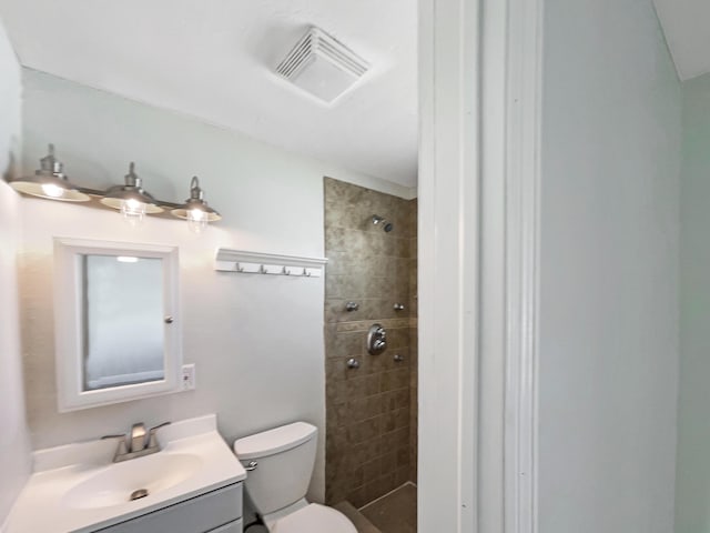 full bath with vanity, toilet, visible vents, and a tile shower