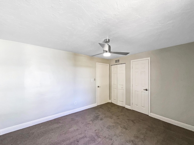 unfurnished bedroom with a textured ceiling, baseboards, dark colored carpet, and multiple closets