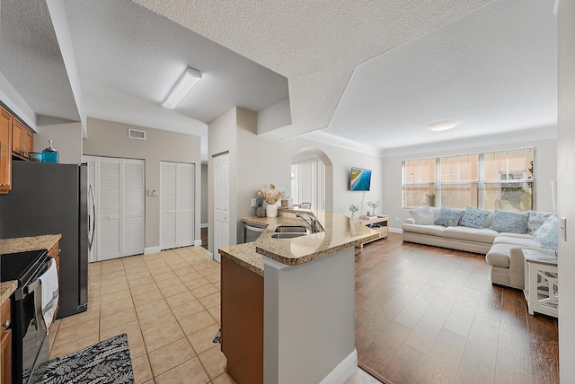 kitchen featuring visible vents, brown cabinets, a sink, stainless steel appliances, and open floor plan