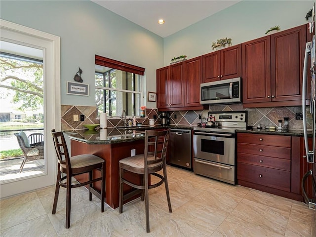 kitchen with tasteful backsplash, dark brown cabinets, a breakfast bar, appliances with stainless steel finishes, and a peninsula