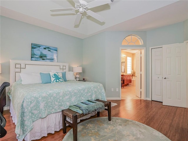 bedroom with baseboards, ensuite bath, wood finished floors, and a ceiling fan