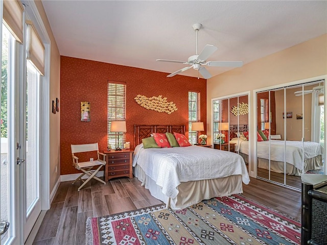 bedroom featuring wood finished floors, baseboards, a ceiling fan, wallpapered walls, and two closets