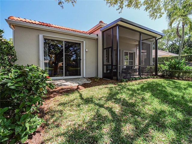 back of property featuring stucco siding, a tile roof, a yard, and a sunroom