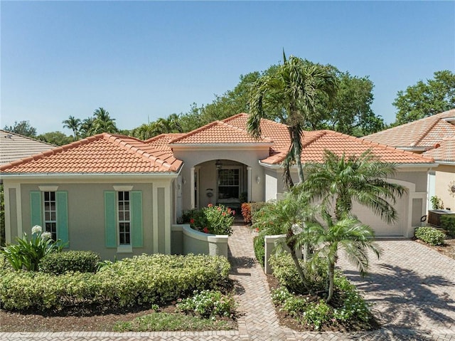 mediterranean / spanish-style house with decorative driveway, a tile roof, an attached garage, and stucco siding