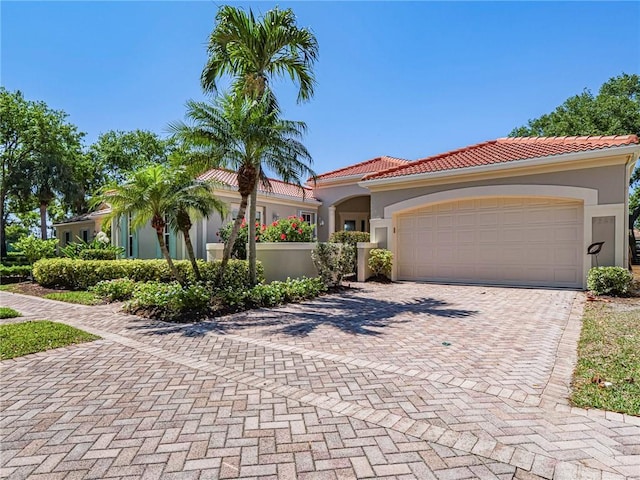 mediterranean / spanish-style home with stucco siding, an attached garage, a tile roof, and decorative driveway