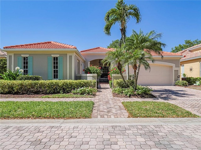 mediterranean / spanish house featuring a tile roof, decorative driveway, a garage, and stucco siding