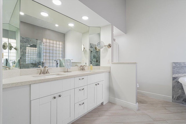 bathroom with double vanity, a stall shower, baseboards, and a sink