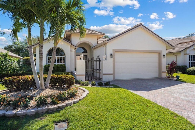 mediterranean / spanish house featuring stucco siding, a gate, decorative driveway, a front yard, and an attached garage