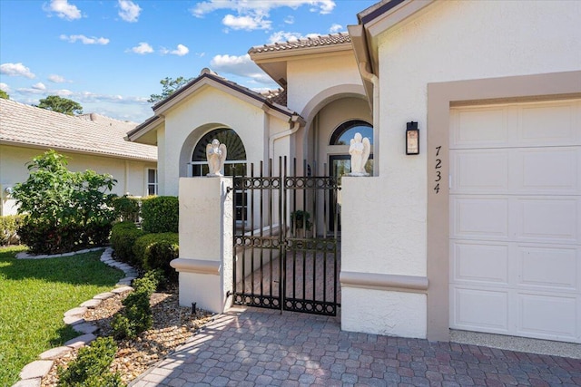 entrance to property with a tiled roof, stucco siding, a garage, and a gate