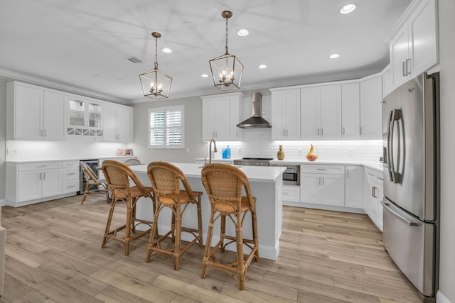 kitchen with ornamental molding, stainless steel refrigerator with ice dispenser, wall chimney range hood, light wood finished floors, and light countertops