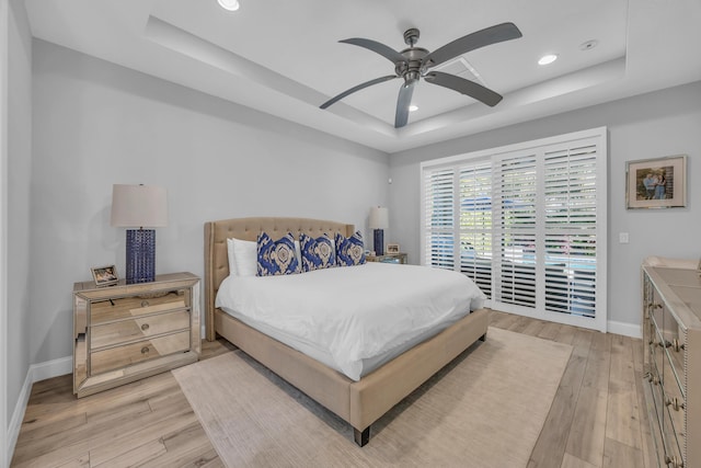 bedroom featuring light wood finished floors, baseboards, a tray ceiling, and access to outside