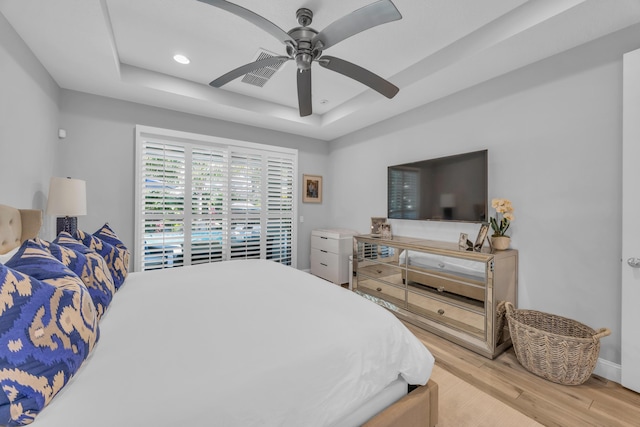 bedroom featuring light wood-style flooring, a tray ceiling, recessed lighting, baseboards, and ceiling fan