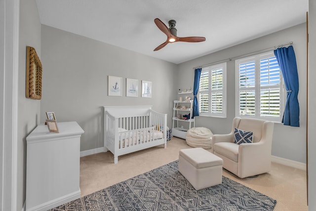 carpeted bedroom featuring a nursery area, baseboards, and ceiling fan