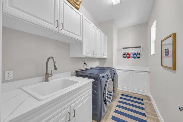 laundry area featuring baseboards, cabinet space, a sink, washer and dryer, and light wood-type flooring