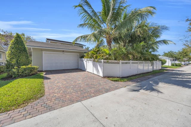 exterior space with an attached garage, decorative driveway, a fenced front yard, and stucco siding