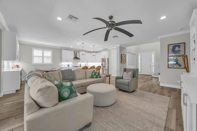 living room with crown molding, light wood-style flooring, a ceiling fan, and visible vents