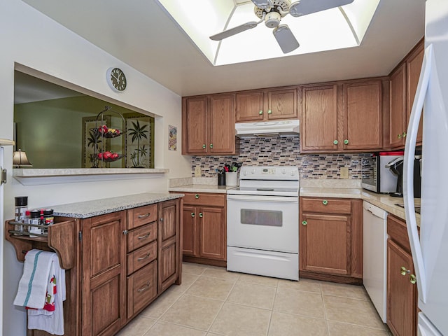 kitchen featuring tasteful backsplash, under cabinet range hood, brown cabinets, light tile patterned flooring, and white appliances