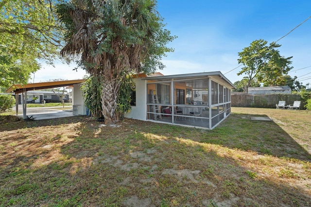 back of property featuring a carport, a lawn, fence, and a sunroom