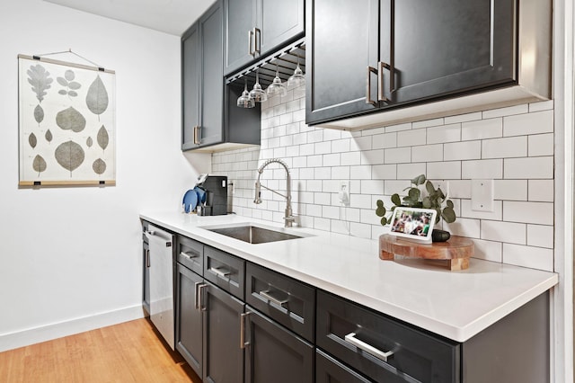 kitchen with light wood finished floors, a sink, light countertops, dishwasher, and tasteful backsplash