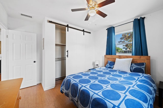 bedroom with visible vents, a ceiling fan, light wood-style floors, and a barn door