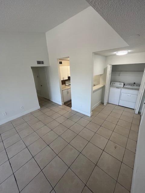 interior space featuring visible vents, lofted ceiling, light tile patterned floors, independent washer and dryer, and a textured ceiling