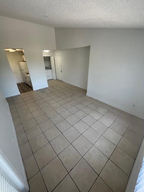 empty room with lofted ceiling, light tile patterned floors, and a textured ceiling