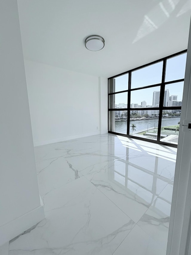 unfurnished room featuring baseboards, floor to ceiling windows, a water view, a view of city, and marble finish floor