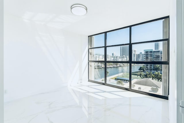 empty room featuring floor to ceiling windows, a view of city, marble finish floor, and a water view