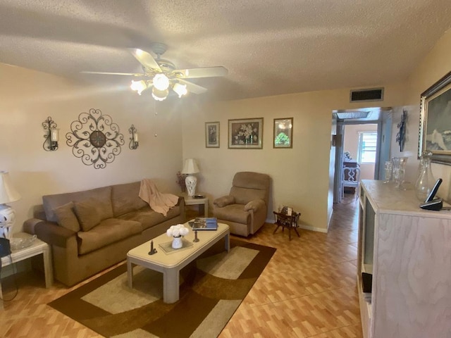 living room featuring visible vents, baseboards, light tile patterned floors, a textured ceiling, and a ceiling fan