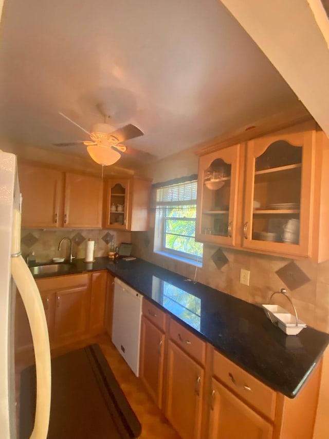 kitchen with dark countertops, white dishwasher, a sink, decorative backsplash, and fridge