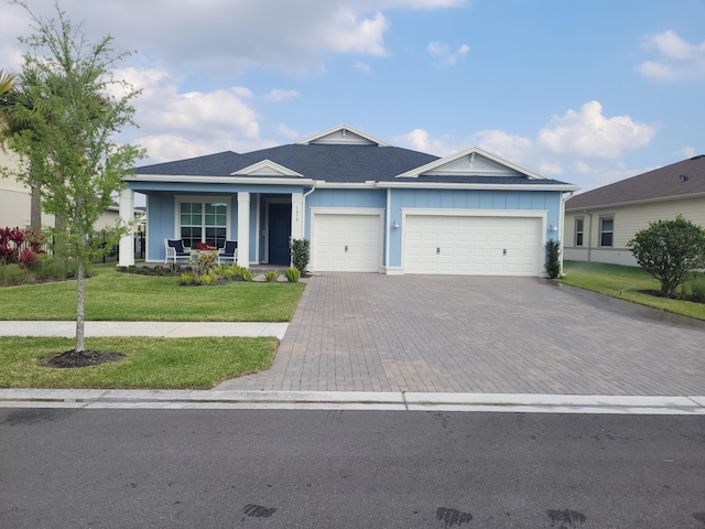 single story home with a front lawn, decorative driveway, a porch, board and batten siding, and an attached garage