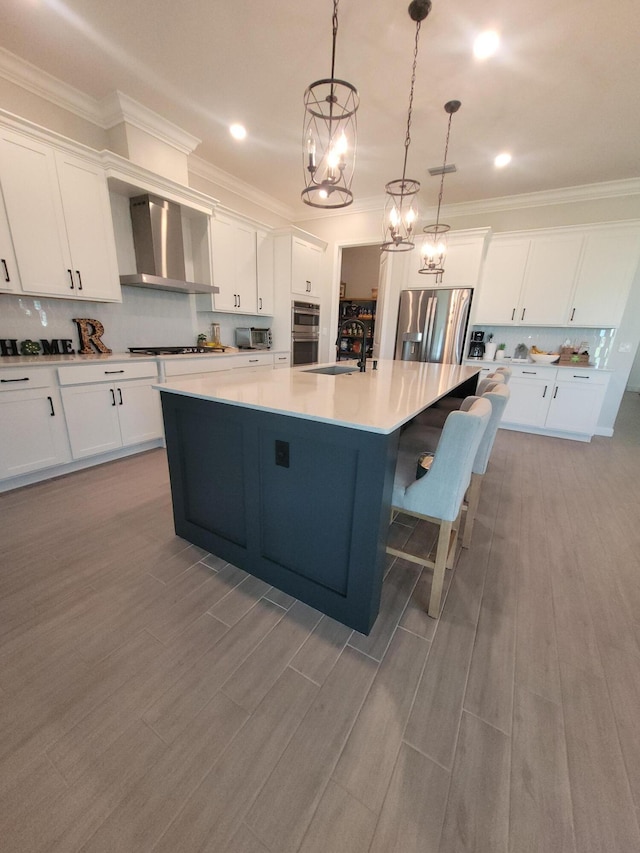 kitchen featuring a spacious island, wall chimney range hood, appliances with stainless steel finishes, white cabinetry, and a sink