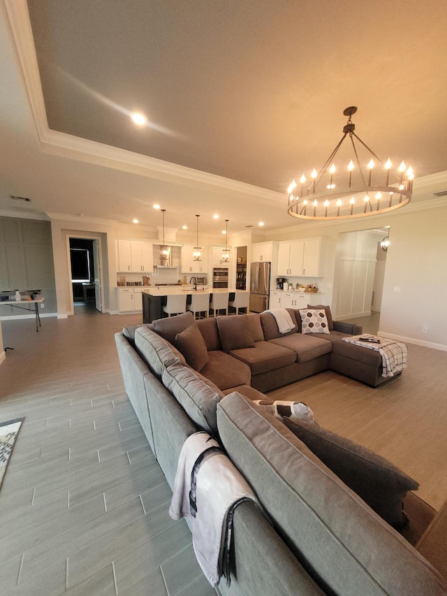 living room with ornamental molding, a tray ceiling, an inviting chandelier, baseboards, and wood tiled floor