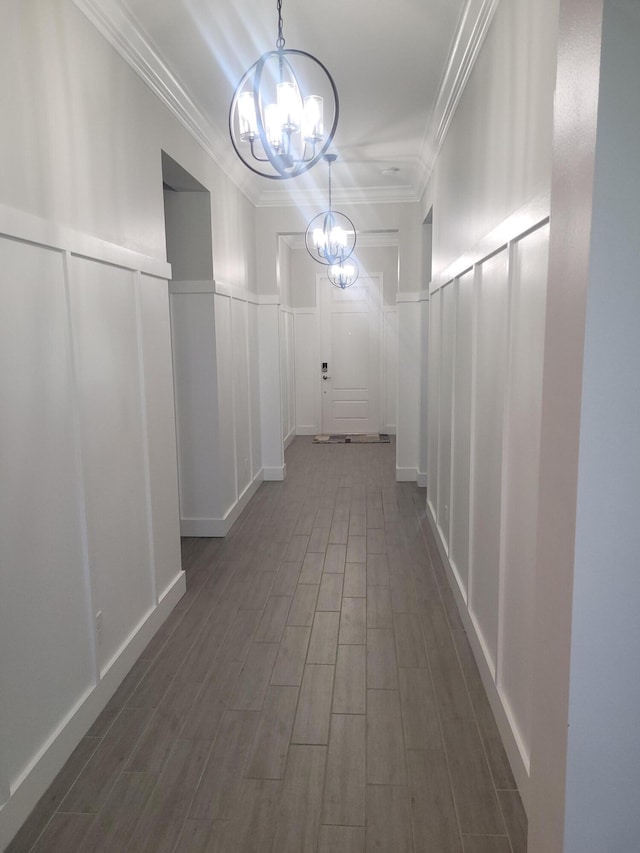 corridor featuring wood finish floors, a chandelier, ornamental molding, wainscoting, and a decorative wall