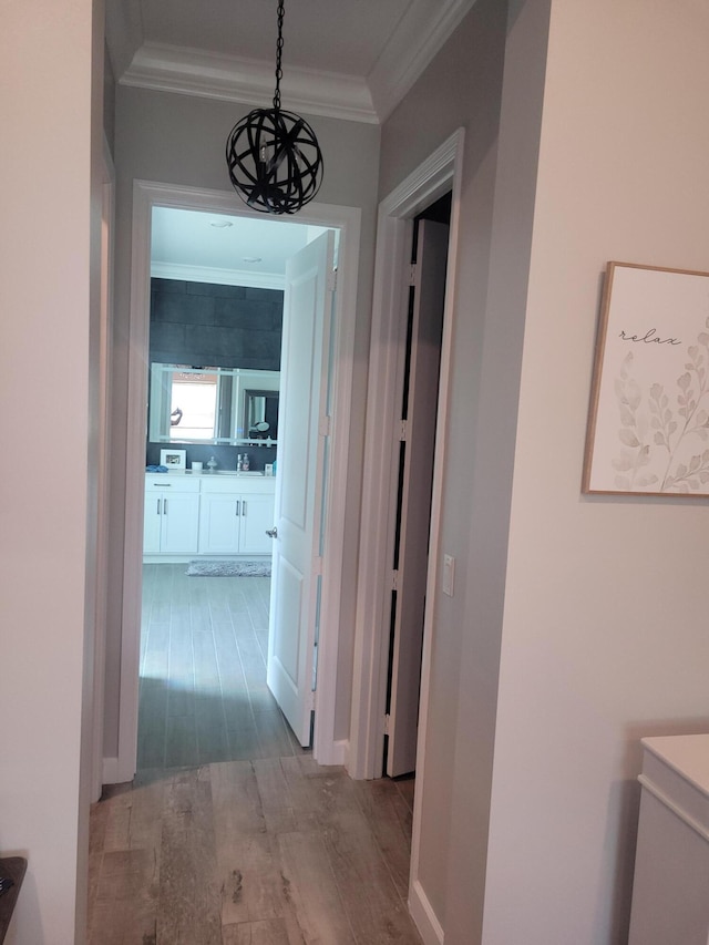 corridor featuring baseboards, wood finished floors, an inviting chandelier, and ornamental molding