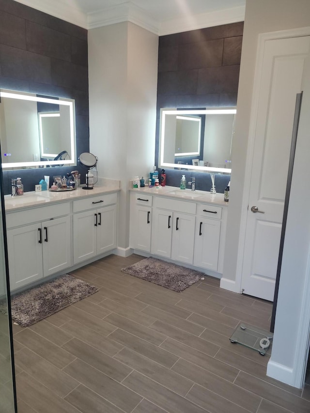 bathroom with crown molding, two vanities, wood finish floors, and a sink