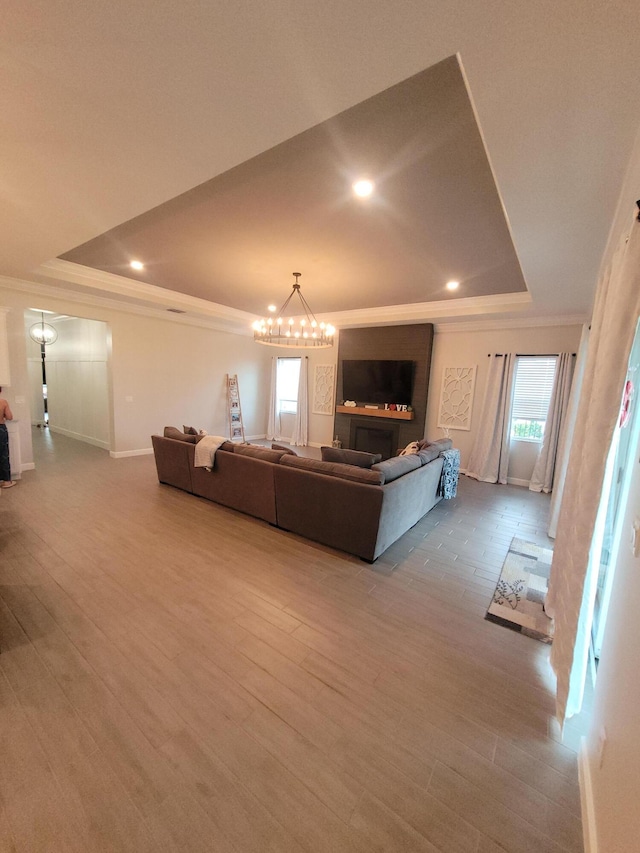 living room with crown molding, a raised ceiling, an inviting chandelier, and wood finished floors