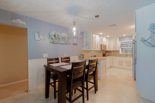 dining area featuring light tile patterned floors, a wainscoted wall, a textured ceiling, and visible vents