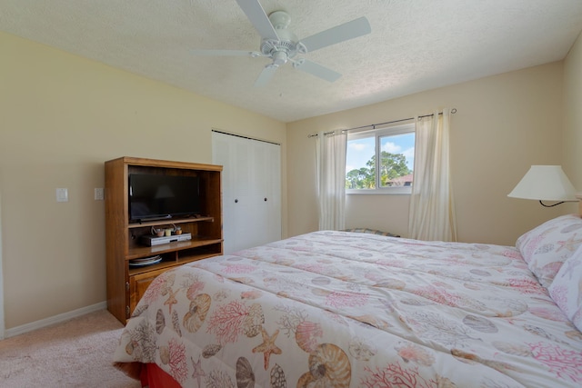 bedroom with a textured ceiling, a closet, baseboards, light colored carpet, and ceiling fan